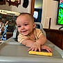 Vanessa joined the competition — help win amazing prizes! baby, high_chair, snack, smiling, indoor, mirror, reflection, person, furniture, table, television, curtains, wood, wall, clothing, hand, face, living_room, home, child