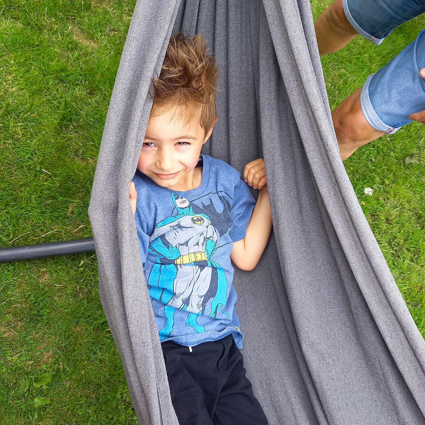 Thibo participe au concours pour gagner de l'argent avec cette photo : batman_tshirt, black_pants, blue_shirt, boy, casual_clothing, child, daylight, denim_shorts, feet, fun, grass, gray_fabric, hammock, outdoor, person, playful, relaxation, smiling, spiky_hair, summer
