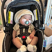 Ander is registered to the contest to win money with this photo: baby, car_seat, pacifier, hat, socks, medical_tape, infant, indoor, person, clothing, black, beige, baby_gear, seated, straps, child, cute, comfort, hospital, equipment