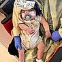 baby, pacifier, sleeping, medical_tape, gloves, handwritten_note, beige_outfit, honeybee_print, socks, infant, child, hospital, chair, yellow_cloth, person, cute, resting, holding, healthcare, comfort