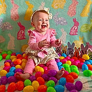 Violet is registered to the contest to win money with this photo: baby, child, smiling, pink_clothing, headband, easter_eggs, colorful, bunny_pattern, blanket, spring, decorations, indoors, happy, cute, festive, sitting, playful, toy, holiday, portrait