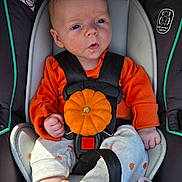 Eilah is registered to the contest to win money with this photo: baby, infant, child, car_seat, orange_clothing, pumpkin, autumn, halloween, harness, safety_seat, portrait, sitting, wide_eyed, surprised_expression, facial_expression, hands, bare_feet, pacifier, indoor, close_up