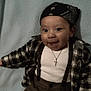 baby, child, smiling, plaid_shirt, bandana, suspenders, cross_necklace, white_shirt, pants, lying_down, blue_blanket, happy, cute, portrait, face, headwear, clothing, infant, person, indoors