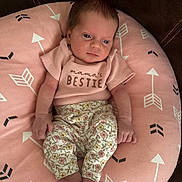Addilynn is registered to the contest to win money with this photo: baby, infant, pink_cushion, arrows_pattern, floral_pants, pink_shirt, text_on_clothing, cute, small_feet, tiny_hands, relaxed, indoor, couch, soft_texture, portrait, newborn, child, person, seated, cozy