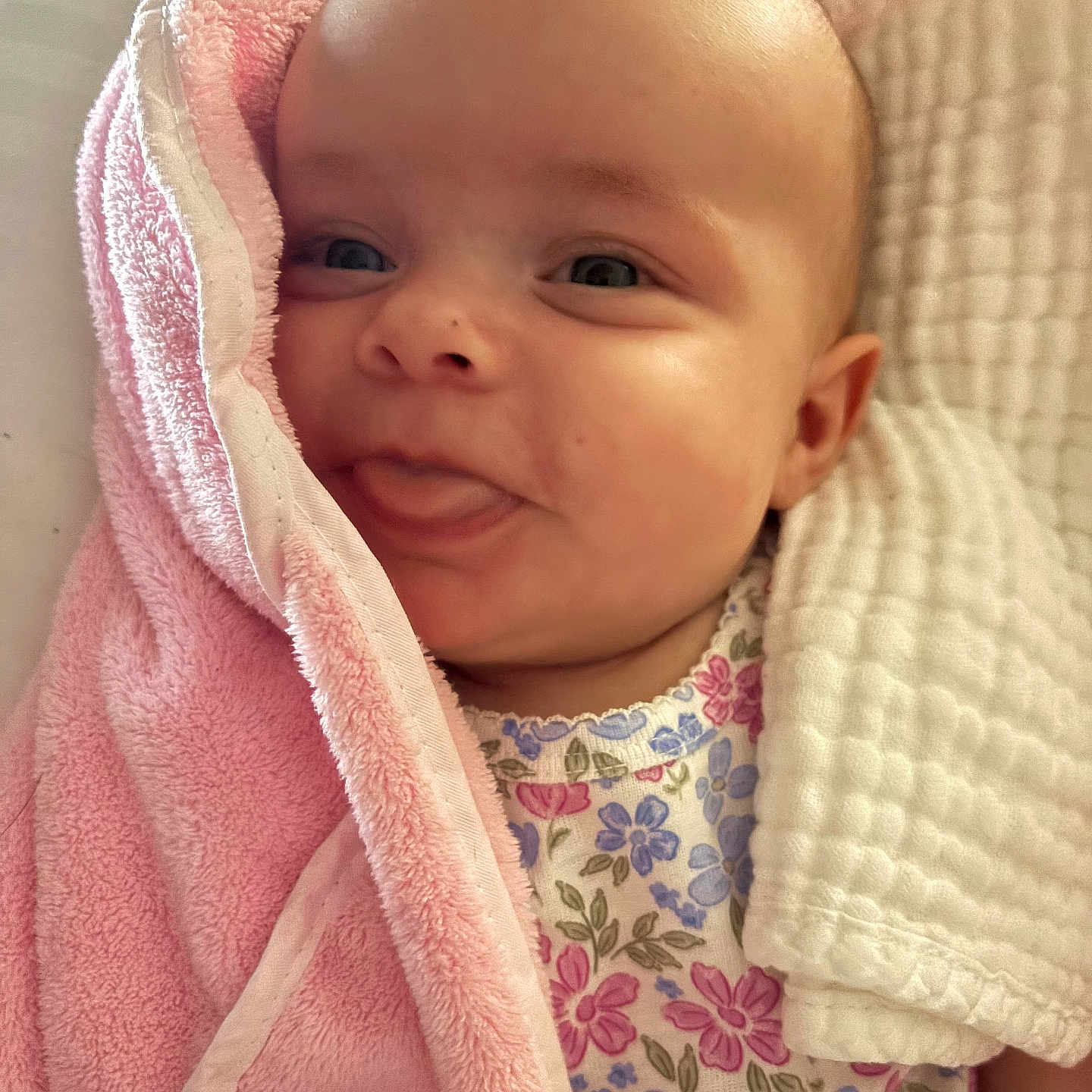 Emmy joined the competition — help win amazing prizes! baby, infant, face, tongue, pink_towel, blanket, floral_clothing, cute, child, person, skin, head, smile, closeup, expression, indoors, soft_texture, wrapped, newborn, adorable