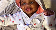 Zariyah joined the competition — help win amazing prizes! baby, child, smiling, hooded_robes, blanket, indoor, cute, happy, portrait, infant, cozy, clothing, person, face, skin, eyes, hand, furniture, bed, fabric
