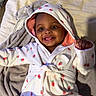 baby, child, smiling, hooded_robes, blanket, indoor, cute, happy, portrait, infant, cozy, clothing, person, face, skin, eyes, hand, furniture, bed, fabric