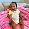 Zariyah joined the competition — help win amazing prizes! baby, infant, smile, happy, couch, blanket, pink_blanket, bib, onesie, pacifier, beaded_clip, curly_hair, topknot, indoors, child, cute, plush, seated, skin, person