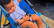 Elijah is registered to the contest to win money with this photo: toddler, child, stroller, blue, yellow, vehicle, sidewalk, outdoor, sunlight, sleeping, baby, person, casual_clothing, footwear, wheel, urban, daytime, relaxing, infant, transport