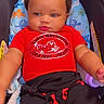 Elijah is registered to the contest to win money with this photo: baby, child, car_seat, red_shirt, black_shorts, blanket, dinosaur_pattern, indoor, cute, infant, smiling, person, portrait, seated, cozy, clothing, young_child, skin, face, head