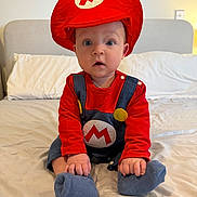 Tommy is registered to the contest to win money with this photo: baby, bed, bedroom, blue_socks, child, clothing, costume, cute, expression, headwear, home, indoors, overalls, person, portrait, red_hat, sitting, soft_lighting, wide_eyes, young_child