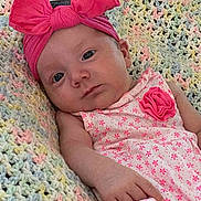 Sophia is registered to the contest to win money with this photo: baby, infant, child, pink_bow, headband, dress, floral_pattern, blanket, knitted_blanket, pastel_colors, laying_down, portrait, cute, indoors, skin, hand, face, expression, young_child, clothing