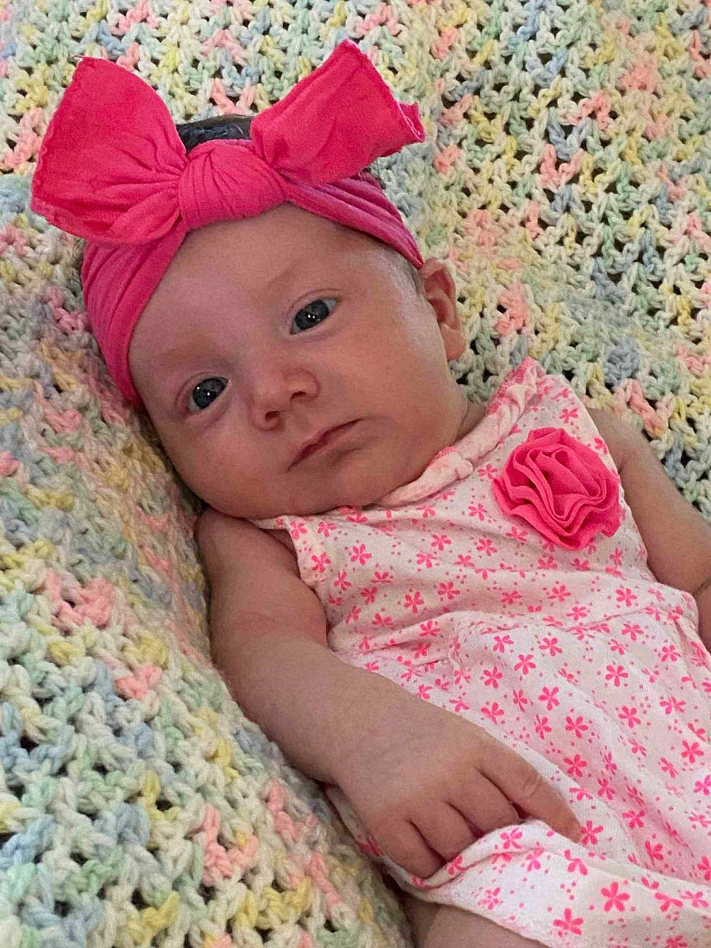 Sophia is registered to the contest to win money with this photo: baby, infant, child, pink_bow, headband, dress, floral_pattern, blanket, knitted_blanket, pastel_colors, laying_down, portrait, cute, indoors, skin, hand, face, expression, young_child, clothing