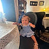 Sophia Grace is registered to the contest to win money with this photo: toddler, child, blue_dress, bow, chair, table, tablecloth, lace, indoor, dining_room, decor, plates, cabinet, lamp, carpet, person, smile, curly_hair, footwear, furniture