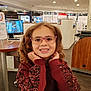 child, girl, glasses, curly_hair, smile, indoors, store, optical_store, table, wooden_table, clothing, red_sweater, portrait, happy, face, person, eyewear, shopping, retail, casual