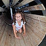 child, girl, curly_hair, smiling, wooden_tunnel, playground, night, crawling, wood, outdoor, fun, happy, play, person, casual_clothing, cute, young, exploration, childhood, leisure