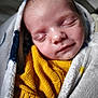baby, sleeping, blanket, yellow_sweater, cozy, closeup, face, infant, soft_texture, peaceful, child, knitwear, wrapped, indoors, portrait, newborn, resting, cute, warm, serene