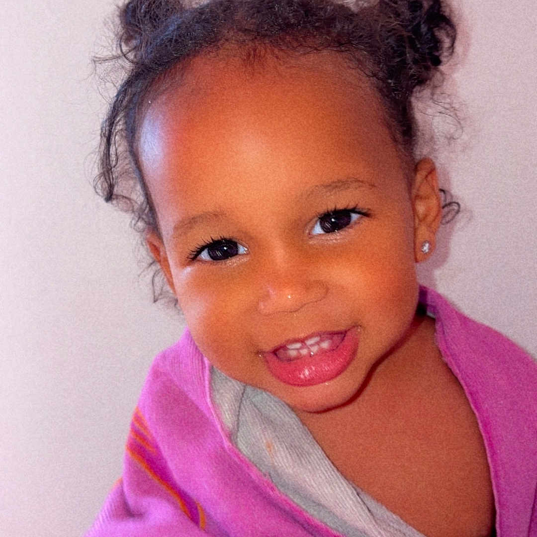 Awa participe au concours pour gagner de l'argent avec cette photo : toddler, child, smile, face, hair_buns, blanket, purple, happy, cute, indoors, portrait, young_child, person, skin, head, eyes, earrings, teeth, warm, cozy