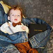Maverick is registered to the contest to win money with this photo: baby, infant, denim_jacket, bow_tie, suspenders, holy_bible, blanket, clothing, portrait, cute, indoor, person, child, soft_texture, lying_down, curious, young, face, fashion, casual