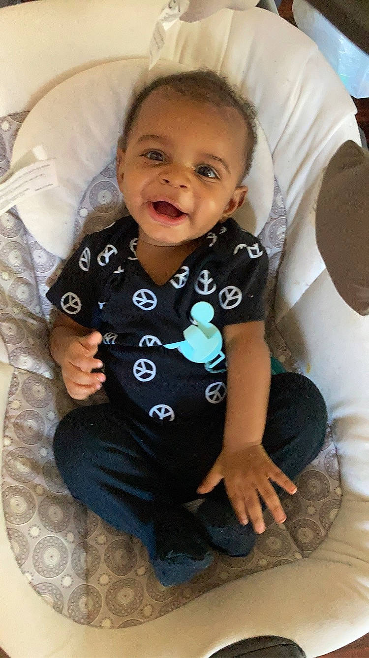 Dallas is registered to the contest to win money with this photo: arm, baby, baby_toddler_clothing, cheek, chin, comfort, eye, finger, gesture, happy, head, human_body, iris, mouth, neck, nose, person, skin, sleeve, smile