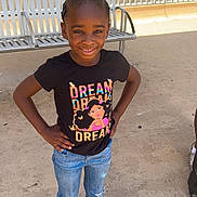 Nayauni is registered to the contest to win money with this photo: child, girl, smiling, standing, hands_on_hips, black_tshirt, graphic_tee, jeans, ripped_jeans, sandals, outdoor, bench, concrete_floor, sunny, building, window, hair_braids, casual_clothing, portrait, happy