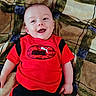 Cylis is registered to the contest to win money with this photo: baby, smiling, red_shirt, puma_logo, black_pants, infant, lying_down, blanket, patterned_blanket, happy, child, cute, portrait, indoors, casual_clothing, baby_face, small_hands, relaxed, bright_colors, young_child