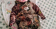 Cylis is registered to the contest to win money with this photo: animal_print, baby, bed, blanket, camouflage, child, clothing, cozy, cute, expression, eyes, face, floral, indoors, infant, lying_down, overalls, pattern, person, soft