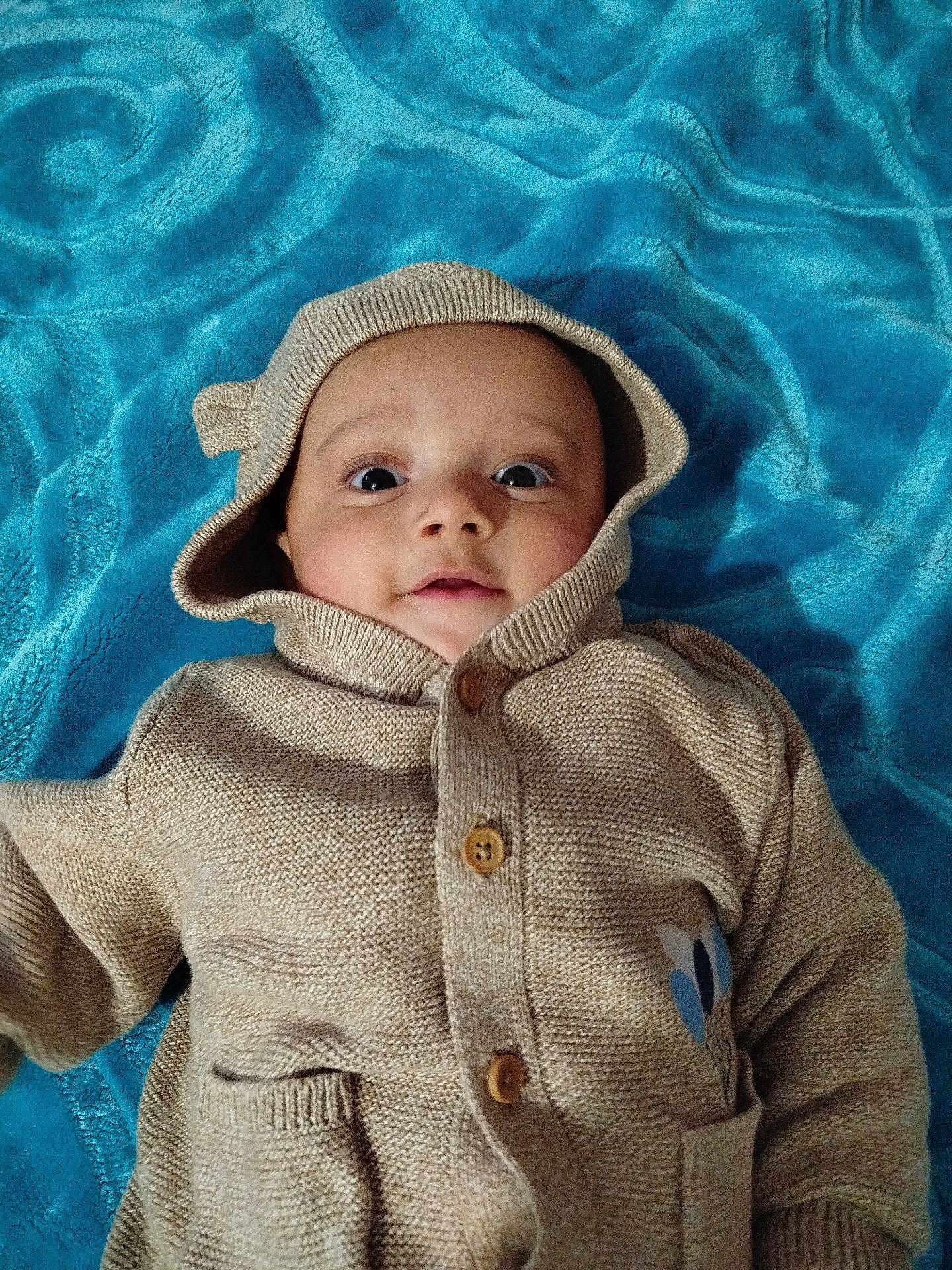 Hassan David participe au concours pour gagner de l'argent avec cette photo : baby, child, hoodie, knitwear, beige, blue_blanket, cute, portrait, face, eyes, infant, laying, cozy, warm_clothing, buttons, pocket, soft_texture, indoors, young, expression