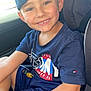 blue_clothing, boy, cap, car_seat, casual, child, closeup, daylight, happy, indoor, person, portrait, seatbelt, shorts, sitting, smile, tshirt, vehicle, window, young