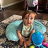 Michael is registered to the contest to win money with this photo: baby, child, blue_pillow, toy, octopus_toy, rug, carpet, indoor, backpack, wooden_floor, curious, sitting, clothing, bib, hand, foot, face, hair, furniture, room
