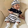 baby, child, smile, hat, striped_clothing, socks, sitting, beige_chair, cushion, cute, infant, portrait, happy, apparel, indoor, comfortable, young_child, person, fashion, casual
