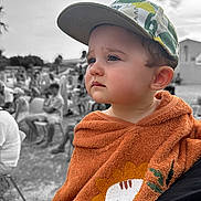 Sandro participe au concours pour gagner de l'argent avec cette photo : child, toddler, cap, orange_towel, lion_design, face, expression, outdoor, people, blurred_background, black_and_white_background, portrait, cute, pensive, clothing, baby, headwear, daylight, person, seated_people