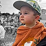 child, toddler, cap, orange_towel, lion_design, face, expression, outdoor, people, blurred_background, black_and_white_background, portrait, cute, pensive, clothing, baby, headwear, daylight, person, seated_people