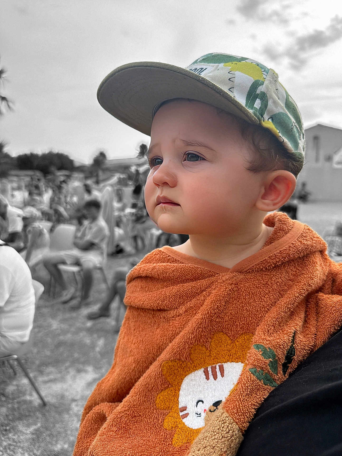 Sandro participe au concours pour gagner de l'argent avec cette photo : child, toddler, cap, orange_towel, lion_design, face, expression, outdoor, people, blurred_background, black_and_white_background, portrait, cute, pensive, clothing, baby, headwear, daylight, person, seated_people