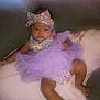 Stormi is registered to the contest to win money with this photo: baby, infant, purple_tutu, headband, clothing, soft_blanket, couch, relaxing, indoors, cute, child, portrait, one_person, sitting, looking_at_camera, baby_girl, legs, feet, fashion, home