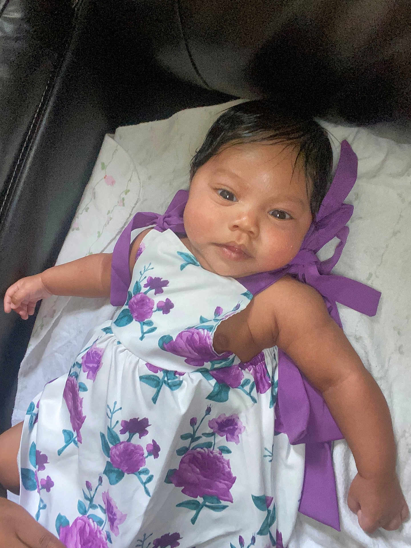Stormi is registered to the contest to win money with this photo: baby, infant, child, dress, floral_pattern, purple, white_blanket, soft_texture, indoor, portrait, cute, skin, hair, lying_down, baby_clothing, child_fashion, person, closeup, young, comfort