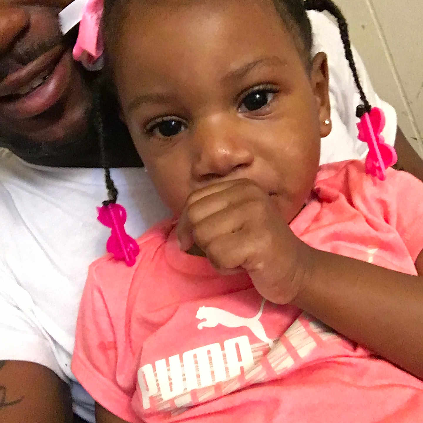 Ti'Amore is registered to the contest to win money with this photo: adult, braids, casual_clothing, child, closeup, cute, face, family, hair_clips, happy, indoors, person, pink_shirt, portrait, puma_logo, seated, skin, smiling, thumb_sucking, toddler