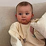 baby, infant, child, sofa, couch, onesie, pacifier, teether, beads, clip, striped_pants, pillow, portrait, indoor, soft_lighting, neutral_wall, rosy_cheeks, curious_expression, sitting, home