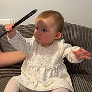 Isla-Rose joined the competition — help win amazing prizes! baby, infant, child, dress, tights, sofa, couch, striped_cushion, hand, arm, holding_object, shadow, wall, indoors, portrait, sitting, cute, playing, fabric, person