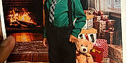 Lester V is registered to the contest to win money with this photo: child, boy, smile, green_shirt, tie, suspenders, teddy_bear, fireplace, christmas, presents, carpet, indoors, holiday, gift_boxes, window, curtains, floor, portrait, shoes, happy