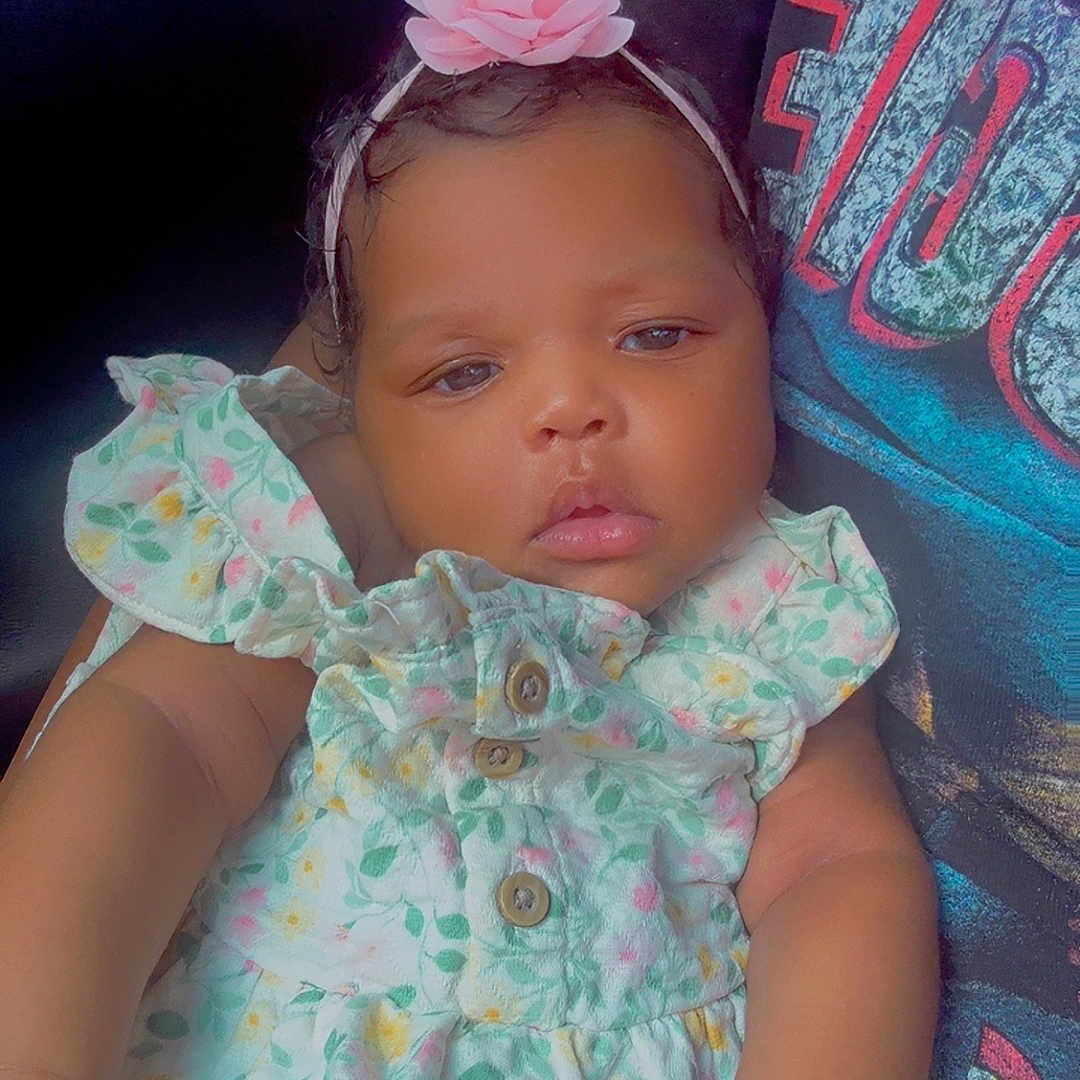 Emora joined the competition — help win amazing prizes! adorable, baby, casual_clothing, child, closeup, comfort, cute, floral_dress, flower_headband, hand, human, indoor, infant, person, portrait, resting, sitting, skin, sleepy, young