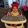 Mia is registered to the contest to win money with this photo: baby, high_chair, red_bow, smile, infant, indoor, furniture, couch, pillow, door, curtain, blanket, happy, child, person, foot, clothing, headwear, home, room