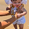 baby, child, sunhat, beach, sand, adult_hands, smile, outdoor, sunlight, summer, feet, shadow, clothing, happy, person, skin, nature, vacation, playful, holiday