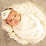 baby, infant, wrapped, blanket, headband, flower, basket, fur, soft_texture, wooden_floor, indoors, portrait, cute, newborn, resting, peaceful, closeup, warm_lighting, comfortable, adorable