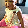 baby, child, smiling, sitting, indoor, pink_leggings, white_top, pacifier_clip, blanket, bow, happy, cute, infant, portrait, young_child, face, skin, hand, leg, clothing
