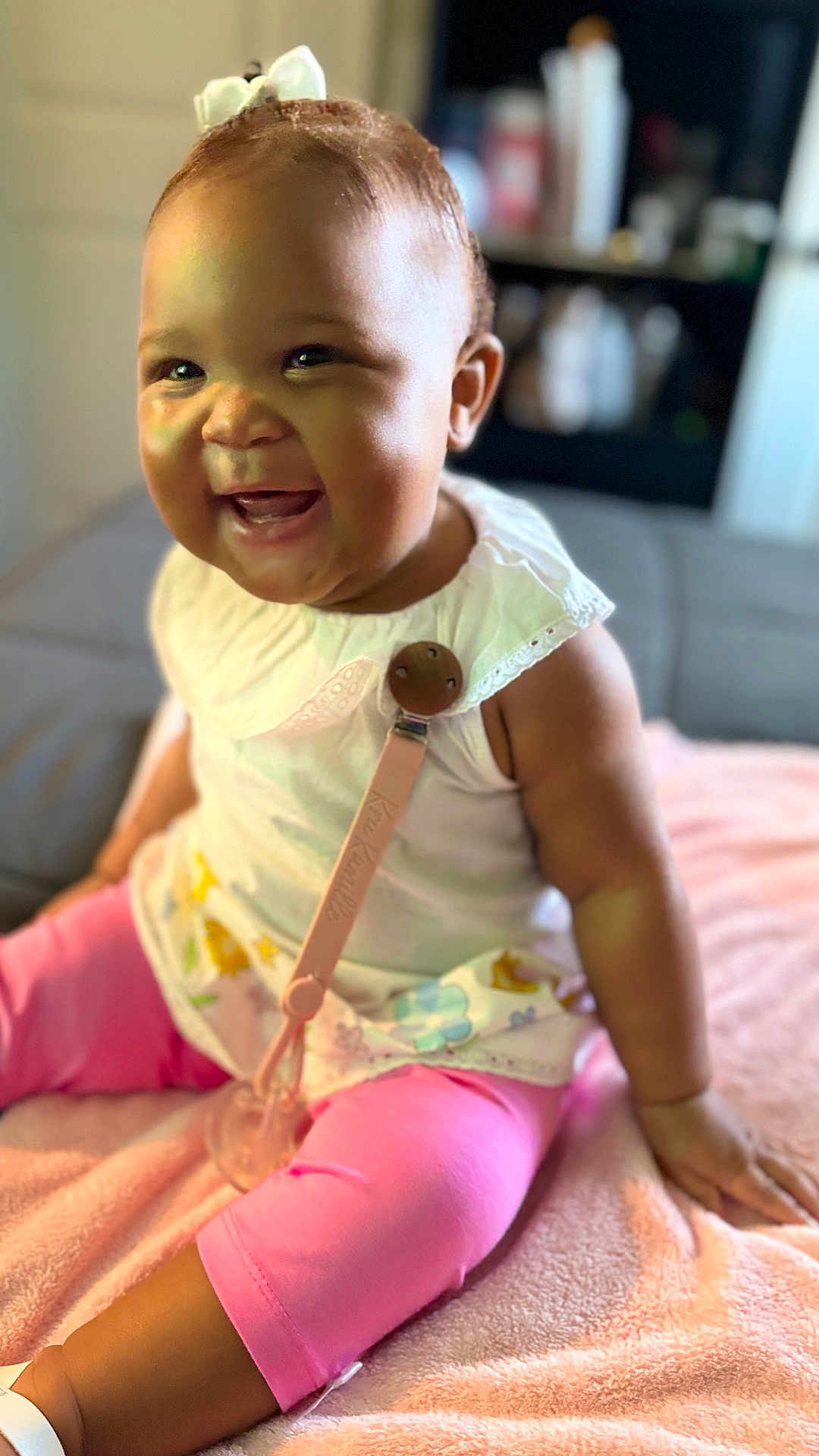 Kru joined the competition — help win amazing prizes! baby, child, smiling, sitting, indoor, pink_leggings, white_top, pacifier_clip, blanket, bow, happy, cute, infant, portrait, young_child, face, skin, hand, leg, clothing