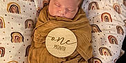 Akari joined the competition — help win amazing prizes! baby, newborn, sleeping, swaddle, cushion, rainbow_pattern, brown_cloth, infant, soft_fabric, peaceful, cute, portrait, child, resting, cozy, wrapped, head, face, indoors, closeup