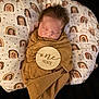 baby, newborn, sleeping, swaddle, cushion, rainbow_pattern, brown_cloth, infant, soft_fabric, peaceful, cute, portrait, child, resting, cozy, wrapped, head, face, indoors, closeup