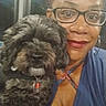 woman, dog, selfie, portrait, glasses, blue_clothing, curly_hair, fluffy_fur, pet, companion, indoors, close_up, smiling, red_lipstick, collar, tag, sitting, shoulder, window, photography
