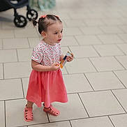 Shéryne participe au concours pour gagner de l'argent avec cette photo : toddler, child, girl, pigtails, pink_skirt, patterned_top, sandals, indoor, floor_tiles, snack, holding, standing, mall, blurred_background, person, cute, young_child, casual_clothing, small_ears, curious